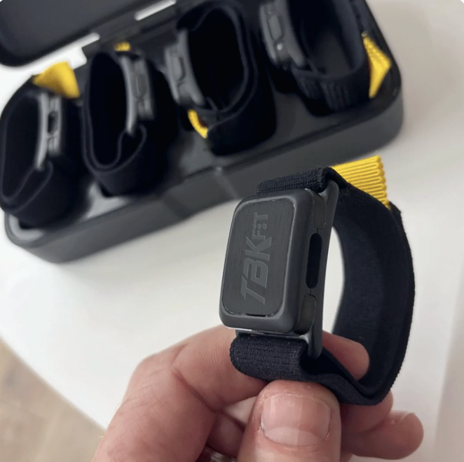 Person holding a black strap with 'TBKFIT' branding in front of a storage case.