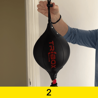Black speed bag with red 'TRIBOXKING' branding held by a person against a neutral background.