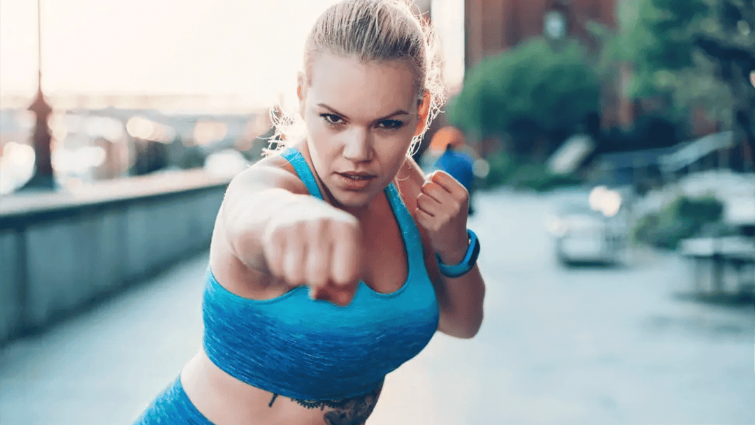 Woman in blue athletic wear posing with fists up in an urban setting